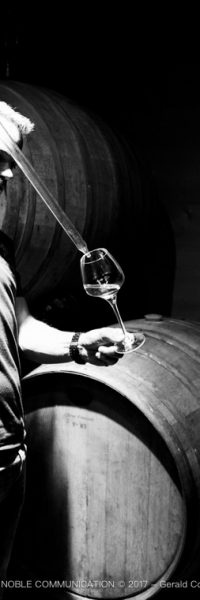 photo d'un homme devant des barriques en train de remplir un verre de vin